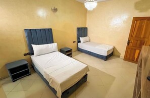 Une chambre avec deux lits, une porte en bois et un lustre.