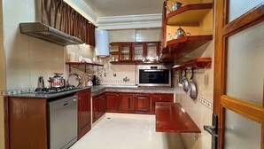 Een keuken met houten kasten, een inbouwoven, een fornuis en een spoelbak.