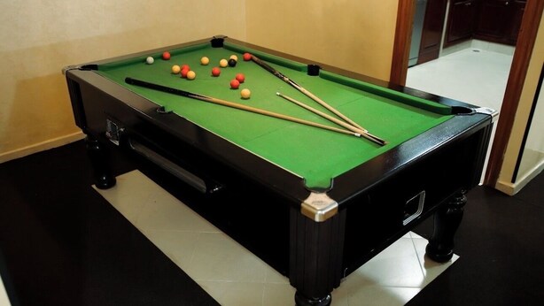 Een pooltafel met ballen en stokken in een kamer met donkere vloeren en houten kasten.
