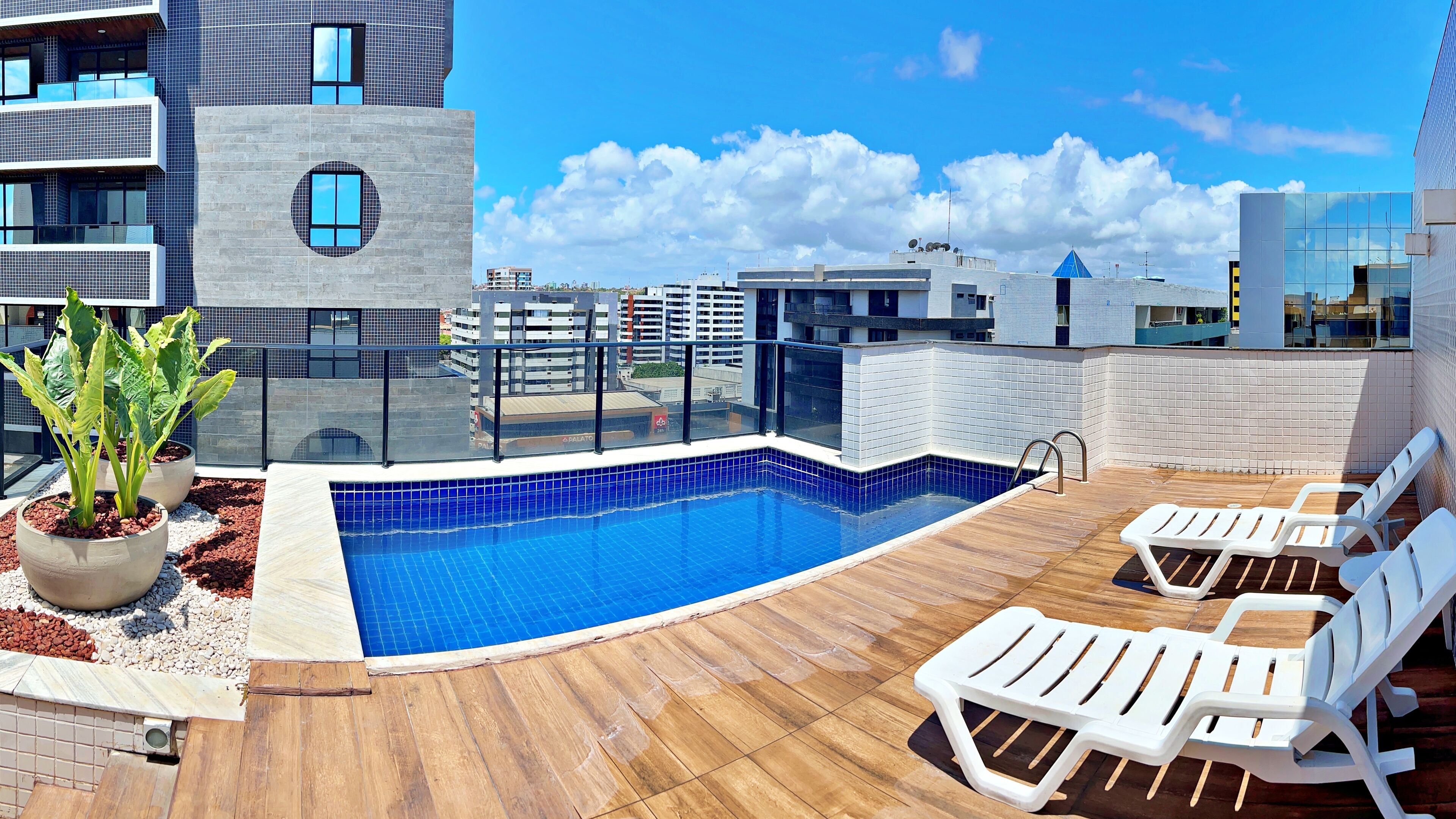 A rooftop pool area with a blue-tiled pool, wooden deck, and white lounge chairs.
