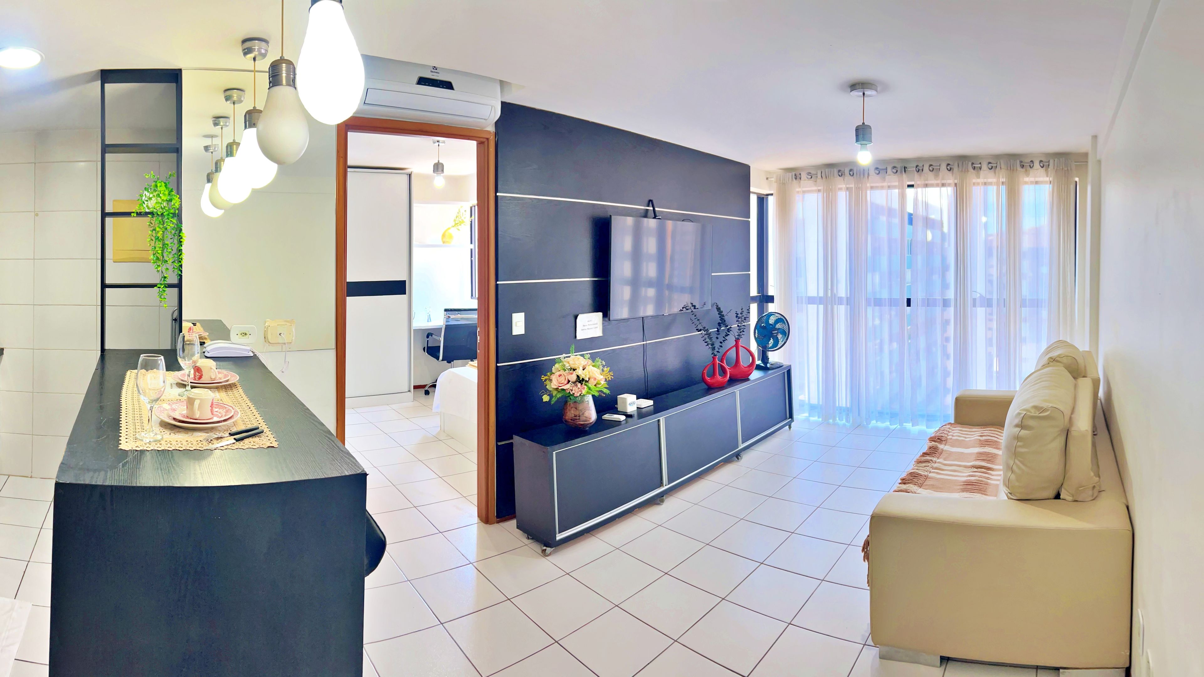 Una sala moderna con un mueble de entretenimiento negro, un sofá beige y un comedor con una mesa dispuesta para dos personas.