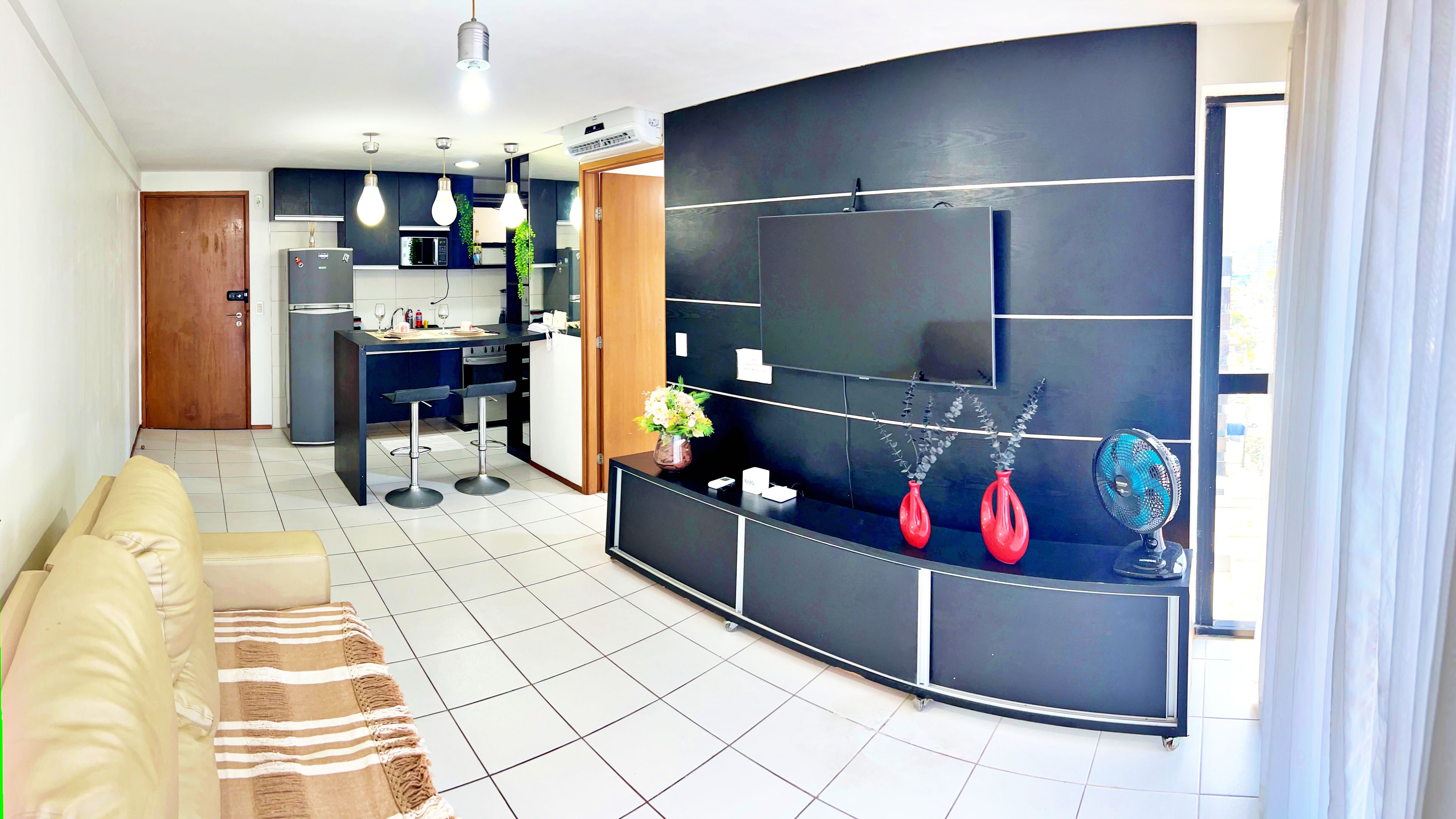 Una cocina moderna con horno empotrado, un comedor con sofá y alfombra a rayas, y una sala de estar con televisor grande y objetos decorativos.