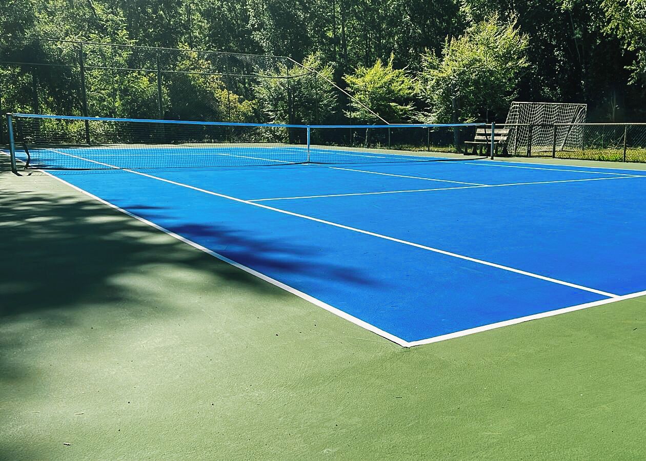 Uma quadra de tênis com superfície azul e área circundante verde.