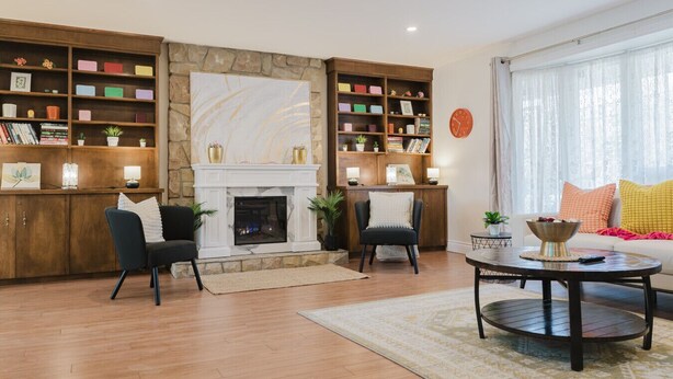 A living room with a fireplace, two armchairs, a coffee table, and bookshelves filled with books and decorative items. - Sydney Retreat | 3BR, 2 Bath Home with Deck & BBQ (Sydney)