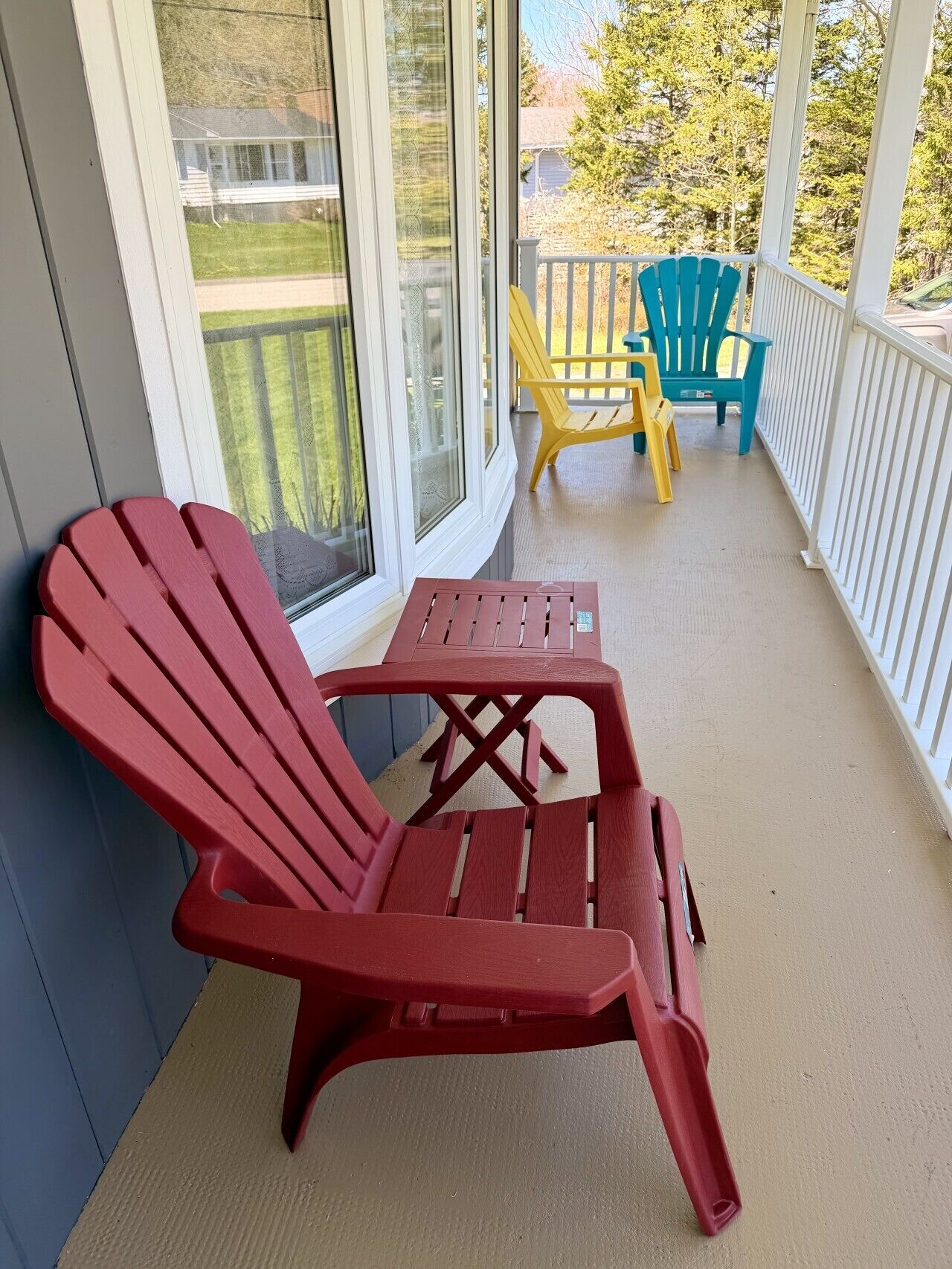 A red Adirondack chair on a covered porch with a view of a green lawn and trees.