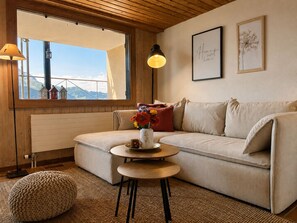 Ein gemütliches Wohnzimmer mit einer Couch, einem kleinen runden Tisch und einem Fenster mit Bergblick.