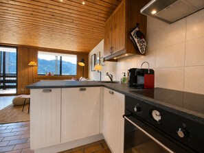 Eine Küche mit Holzbalkendecke, einem großen Fenster und einem eingebauten Backofen.