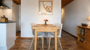 Un coin repas avec une table et des chaises en bois, une œuvre d’art encadrée au mur et une cuisine en arrière-plan.