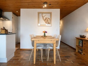 Ein Essbereich mit Holztisch und -stühlen, einem gerahmten Kunstwerk an der Wand und einer Küche im Hintergrund.