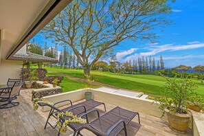 En overdækket terrasse med udendørs møbler, udsigt til en golfbane og et stort træ.
