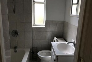 A small bathroom with a bathtub, toilet, and sink. - Cozy 1-bedroom apartment in cool Astoria with AC (Astoria)