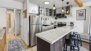 Una cocina moderna con armarios blancos, una isla grande con taburetes de bar, electrodomésticos de acero inoxidable e iluminación colgante.