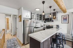 A modern kitchen with white cabinets, a large island with bar stools, stainless steel appliances, and pendant lighting. - Lake Dillon Views! Sunny Ski Days & Spring Fun (Dillon)