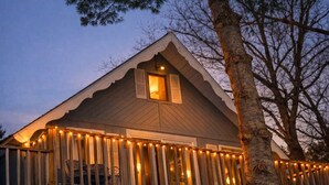 A house with a gabled roof, a visible window, and a porch with string lights. - Clam Lake Waterfront Cottage w/ Kayaks (Bellaire)