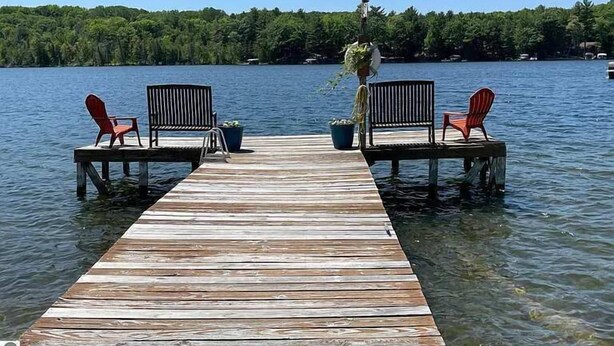 A wooden dock extending into a lake with two red Adirondack chairs and a bench at the end. - Clam Lake Waterfront Cottage w/ Kayaks (Bellaire)
