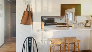 A modern kitchen with white cabinetry, a copper faucet, and a wooden island with stools. - Clam Lake Waterfront Cottage w/ Kayaks (Bellaire)