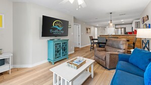 A modern living room with a television, a blue sofa, a brown recliner, and a white coffee table. - Gulf View~Steps to Sugar White Sands~Pool~Tennis~Private Beach Access~Ciboney 2011 (Destin)
