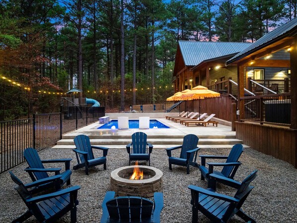 Ein Poolbereich mit Adirondack-Stühlen, einer Feuerstelle und einer Holzterrasse.