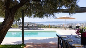 Zona de piscina con vistas a la ciudad y montañas, mobiliario exterior y mesa lista para comer.
