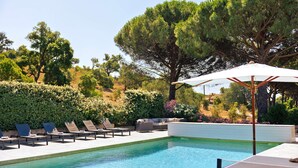 A pool area with lounge chairs and an umbrella, surrounded by greenery and trees. - Villa for 15 people - Private pool - Air conditioning - WiFi - Sainte Maxime - 5-star rated (STE MAXIME)