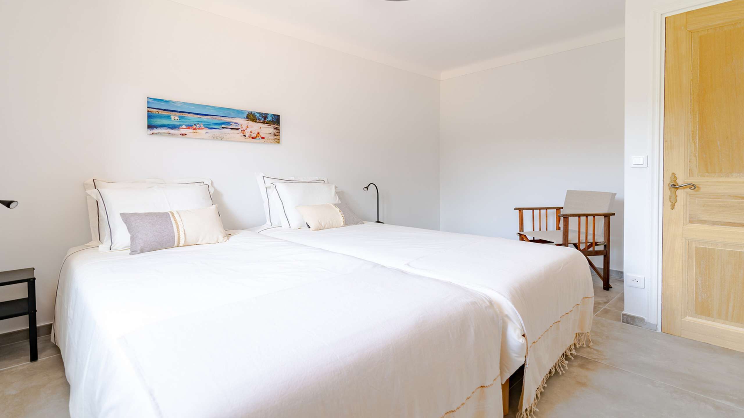 A bedroom with a large bed, a bedside table, a chair, a desk, and a door.