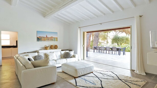 A modern living room with a sofa, ottoman, and a dining area visible through a glass door. - Villa for 15 people - Private pool - Air conditioning - WiFi - Sainte Maxime - 5-star rated (STE MAXIME)