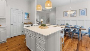 Una cocina con isla central, muebles blancos y un comedor con sillas azules.