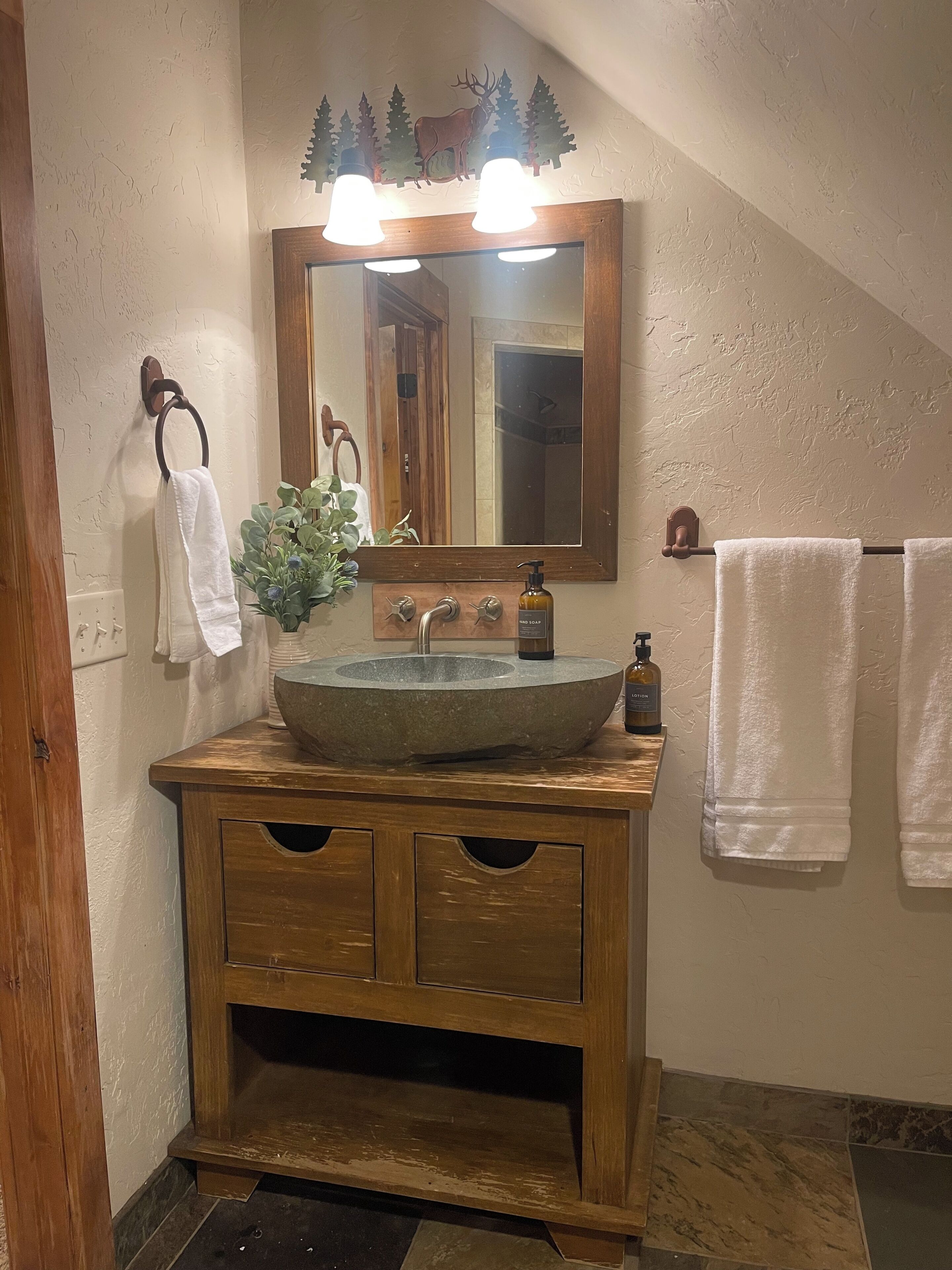 A bathroom with a wooden vanity, a large mirror, and a stone sink.