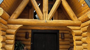 A log cabin with a black door, wooden beams, and a welcome mat.