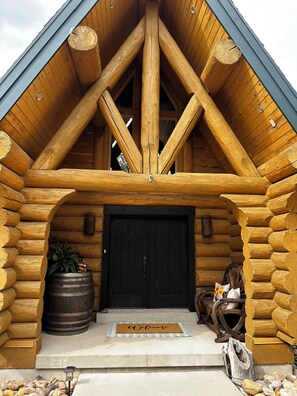 Una cabaña de troncos con puerta negra, vigas de madera y felpudo.