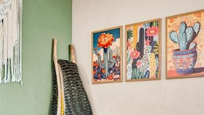 Olohuone, jossa on vihreä seinä, harmaa sohva värikkäillä koristetyynyillä, makrame-seinävaate ja kolme kehystettyä kaktusaiheista taulua.