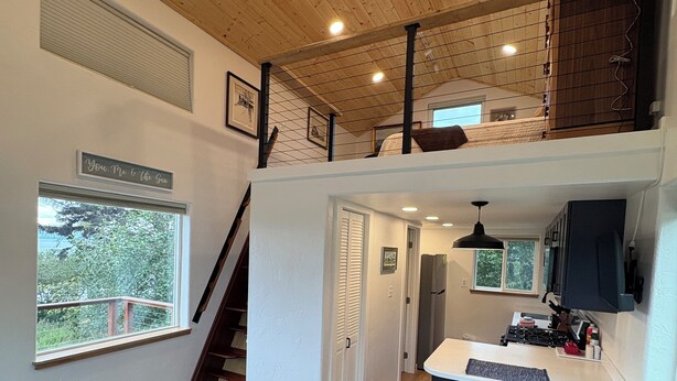 Un vaste espace de vie aménagé en loft, comprenant une cuisine, un escalier menant à un niveau supérieur et une vue sur la verdure environnante.