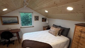 Une chambre avec un plafond en bois, un lit recouvert d’une courtepointe, un bureau avec une chaise et une commode.