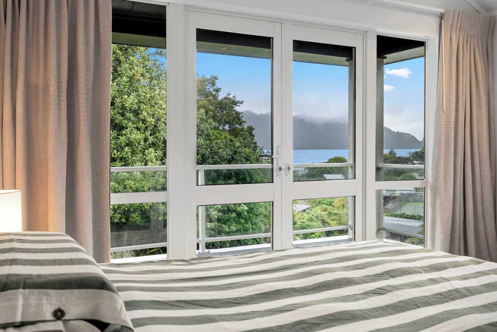 A bedroom with a large window, a bed with striped bedding, and curtains.
