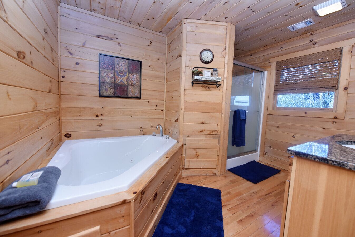 A wooden cabin bathroom with a bathtub, a shower, a clock, and a window.