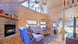 Indbydende interiør i en hytte med en stenspir, en sofa, et spisebord og et køkkenområde.