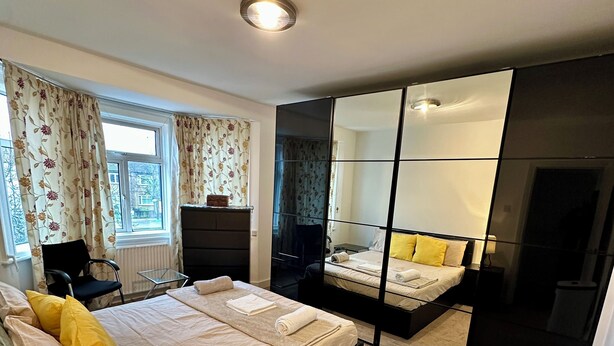 Quarto moderno com uma cama grande, uma mesinha de cabeceira com abajur, guarda-roupa e lixeira.
