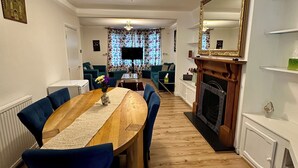 Uma sala de jantar com uma mesa de madeira e cadeiras azuis, uma televisão e uma lareira.