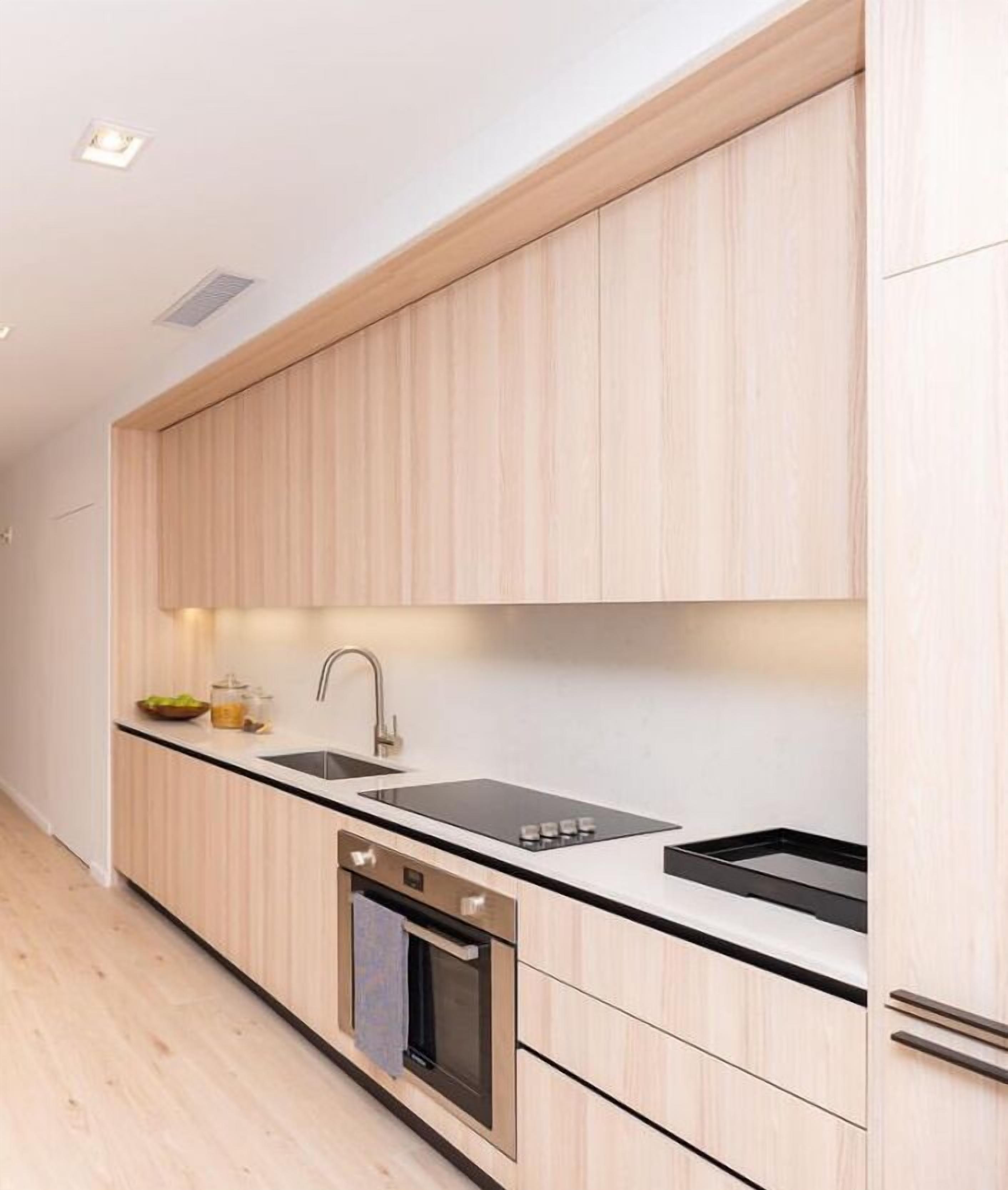 A modern kitchen with light wood cabinetry, a black countertop, stainless steel appliances, and a built-in oven.