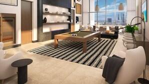 A modern living room with a pool table, comfortable seating, and large windows offering a city view. - King Deluxe Studio (Miami)