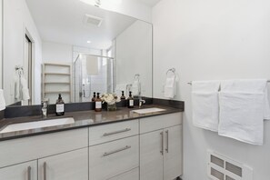 Une salle de bain moderne avec un grand miroir, deux lavabos et un espace douche.