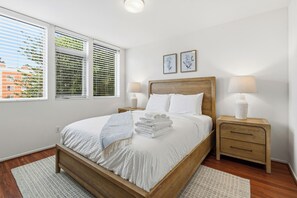 Un lit bien fait, avec du linge de lit blanc, deux tables de chevet avec des lampes et une fenêtre avec des stores.