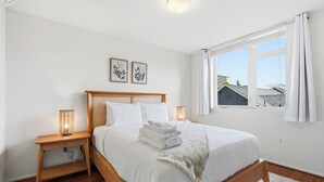 A neatly made bed with white linens and a folded towel, a bedside lamp, and a small wooden nightstand. - Rooftop Retreat w/ Stunning Views | Ballard Gem (Seattle)
