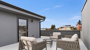 A rooftop terrace with wicker furniture and a glass door. - Rooftop Retreat w/ Stunning Views | Ballard Gem (Seattle)