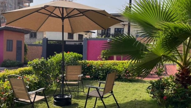 Ein Sitzbereich im Freien mit Tisch und Stühlen, einem großen Sonnenschirm und einer Palme.