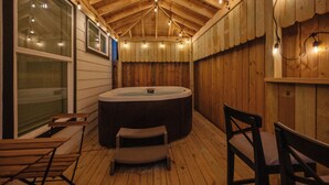 Una terraza de madera con un jacuzzi, sillas de madera y luces colgantes.
