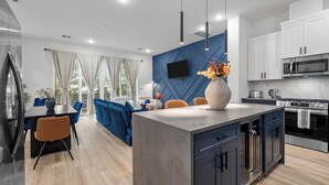 Una cocina moderna con una isla central, electrodomésticos integrados y una zona de comedor con mobiliario azul.