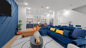 Una sala de estar moderna con un sofá modular, una mesa de centro y una cocina al fondo.