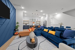 Ein modernes Wohnzimmer mit einem Ecksofa, einem Couchtisch und einer Küchenzeile im Hintergrund.