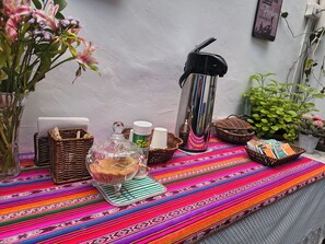 A table with a colorful woven tablecloth, a glass decanter, a thermos, and a basket of books. - Hostal Flor de Loto  (Cusco)